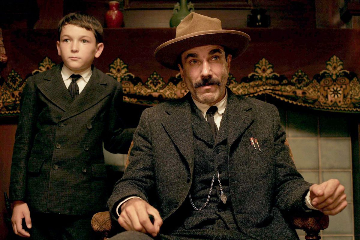 Dillon Freasier stands next to a seated Daniel Day Lewis in a screenshot from There Will Be Blood