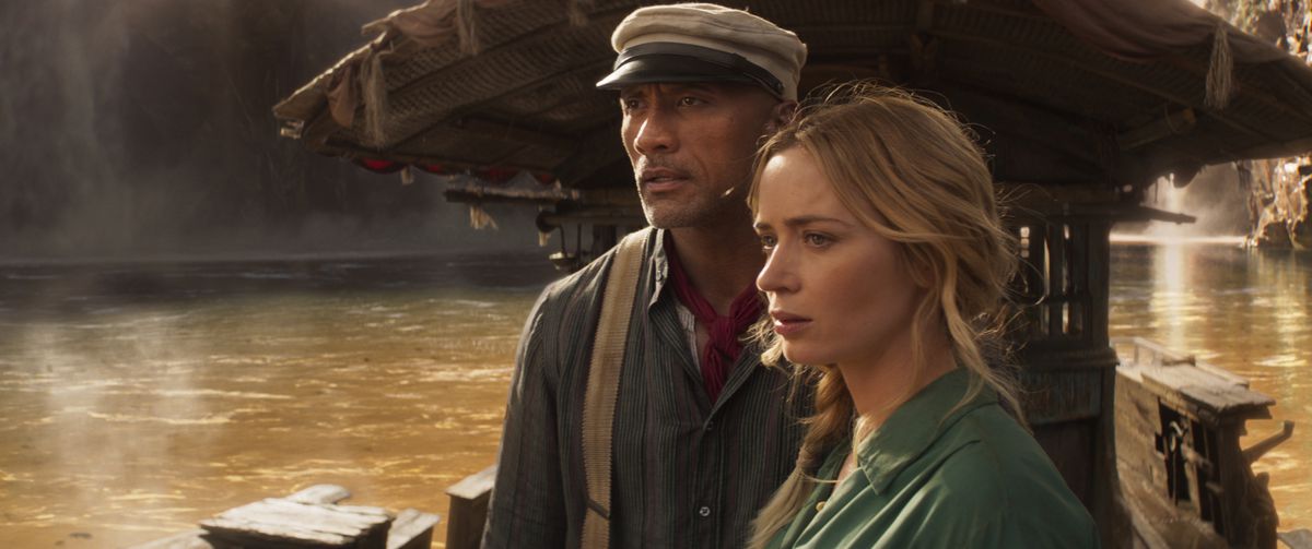 Dwayne Johnson in a hat and Emily Blunt look off their ship in Jungle Cruise