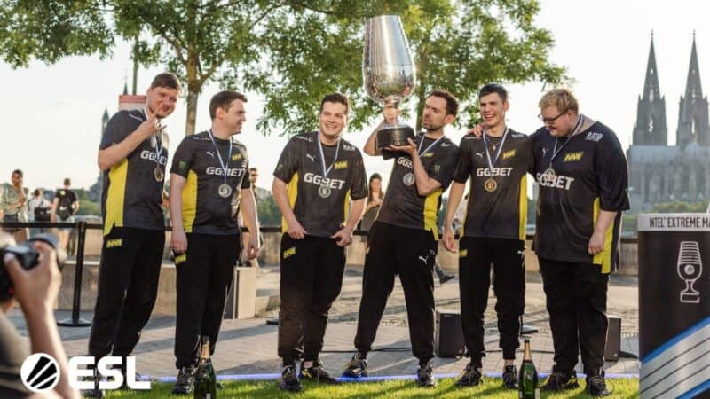 The Natus Vincere CS:GO team poses together outside with a large trophy after winning an event.