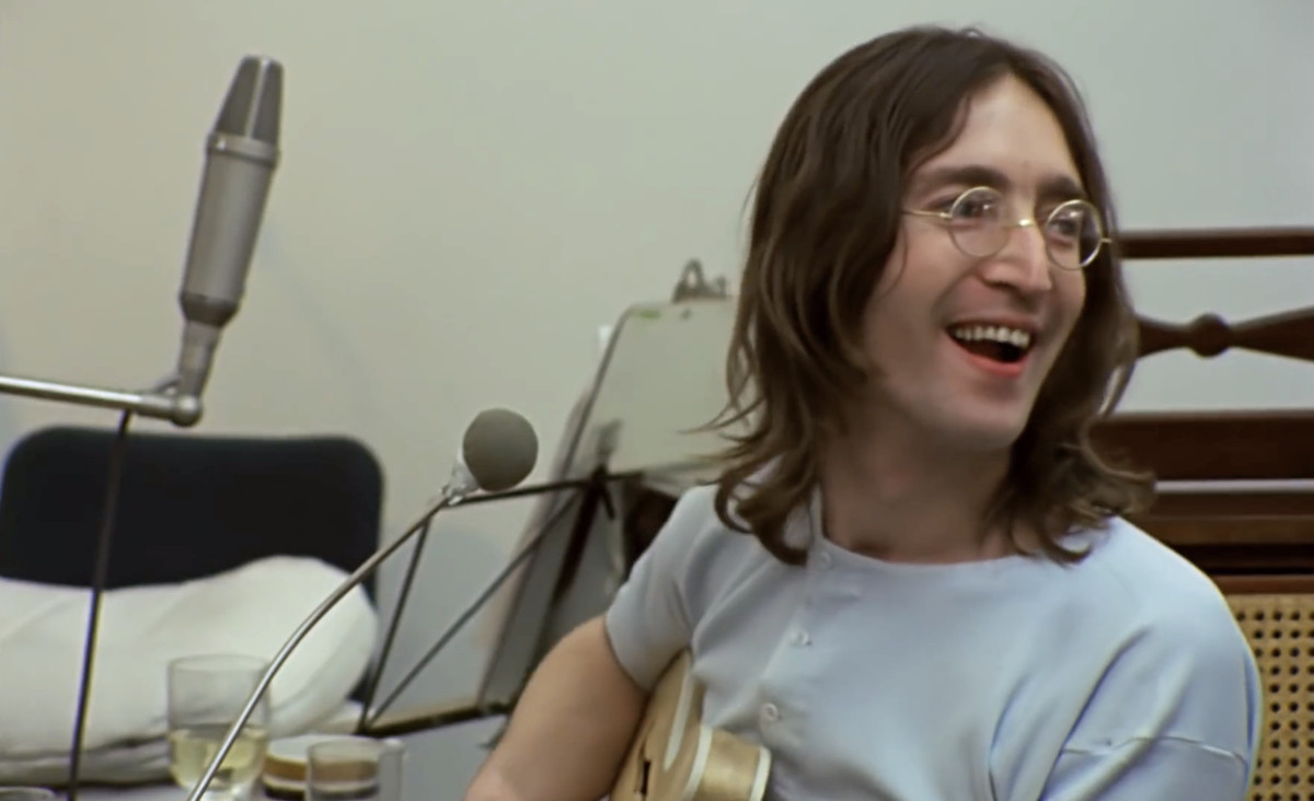 a young John Lennon at the microphone of a recording session, with guitar, in 1969