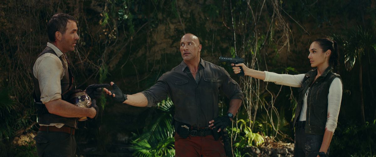 Gal Gadot holds Ryan Reynolds at gunpoint while Dwayne Johnson tries to get him to surrender a golden egg in Red Notice