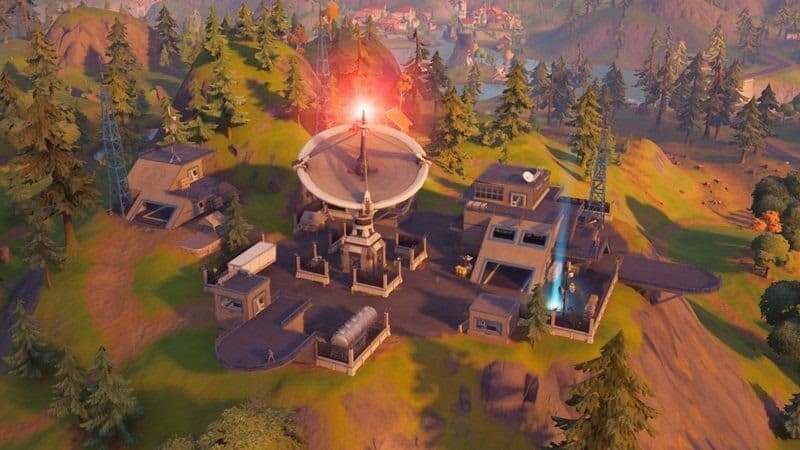 A large satelite dish on the roof of a building emits a glowing red light at one of the IO Bases from Fortnite, Chapter 2