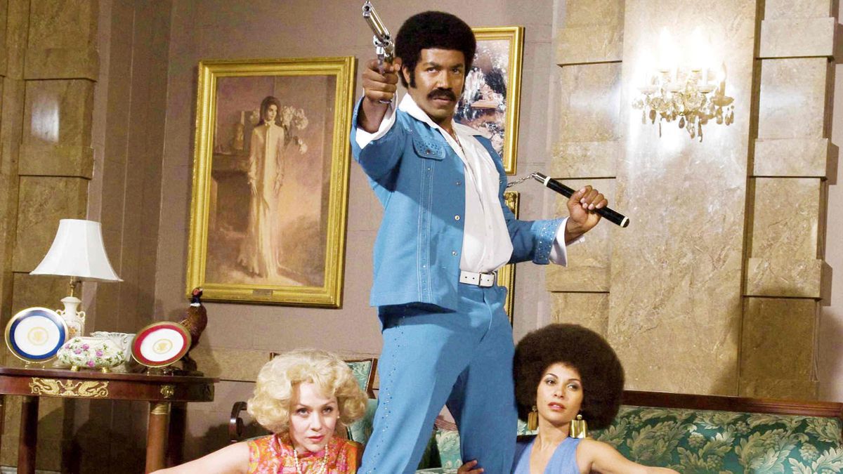 Black Dynamite posing with a pistol and nunchucks.