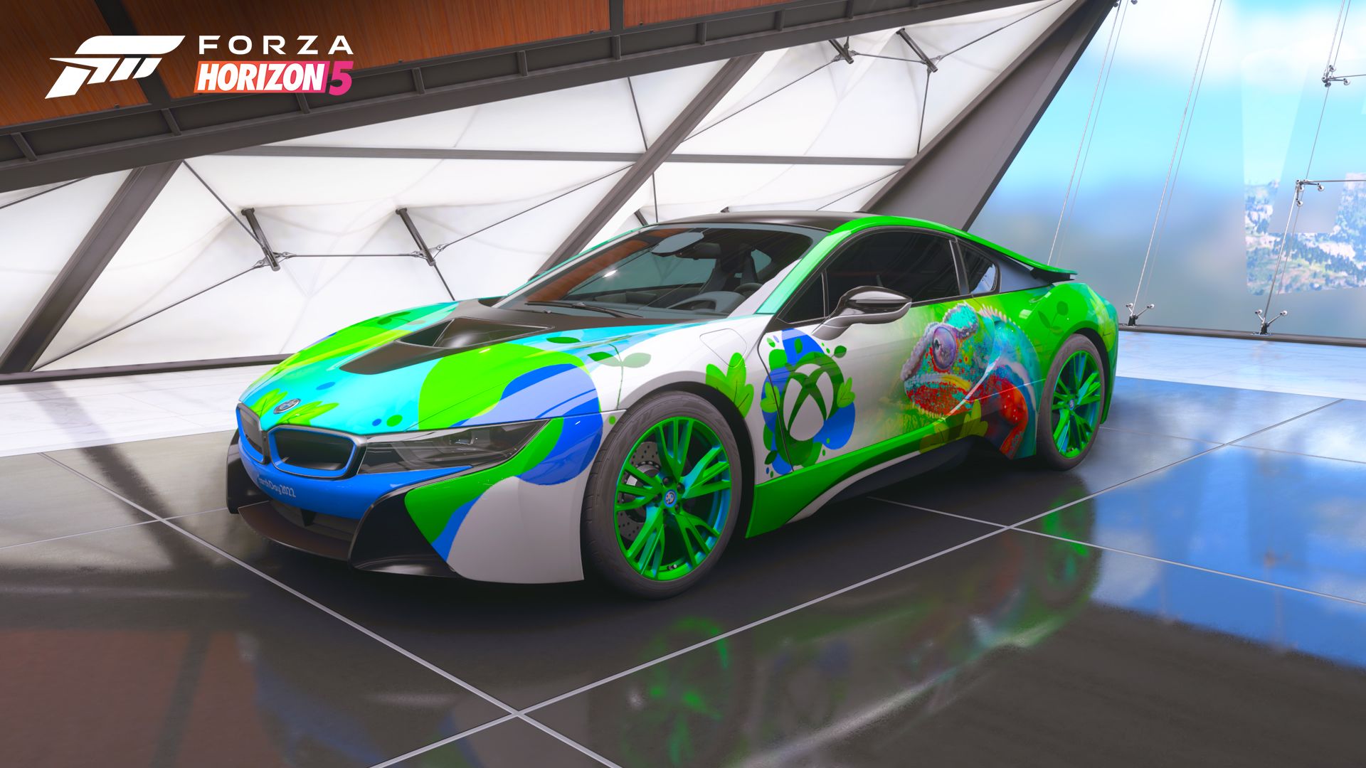 A 2015 BMW i8 car sits inside a sleek, professionally lit garage at the Mexico Horizon Festival. The car is painted in hues of blue, green, and white with shapes suggesting plant foliage. The Xbox logo is visible on the side of the car, next to a detailed image of a chameleon in similar hues.