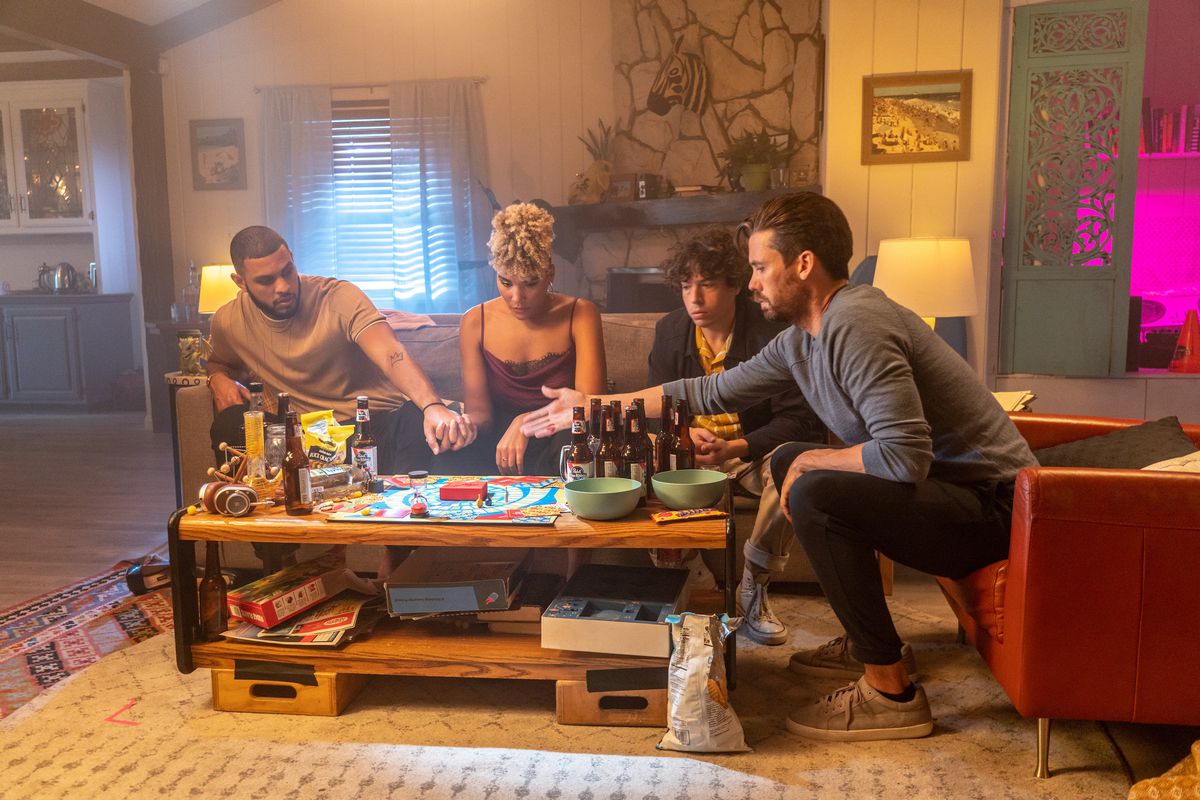 The cast of GATLOPP, huddled around their board game on a coffee table covered in beer bottles and snacks