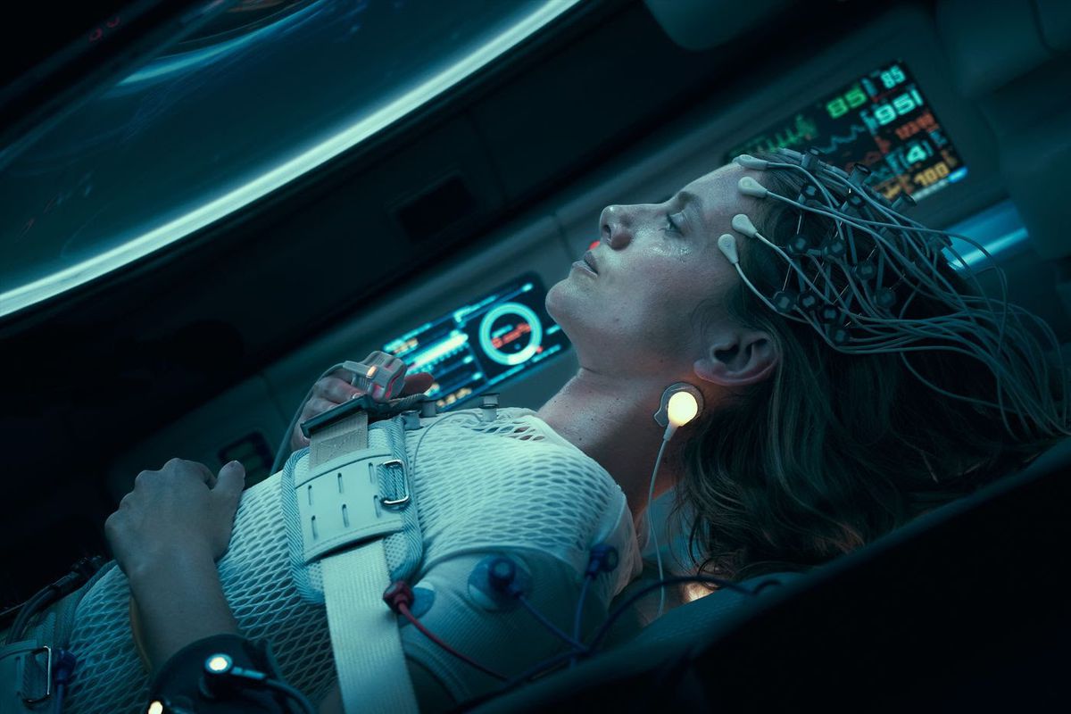 A woman in a cryosleep chamber with diodes attached to her forehead.