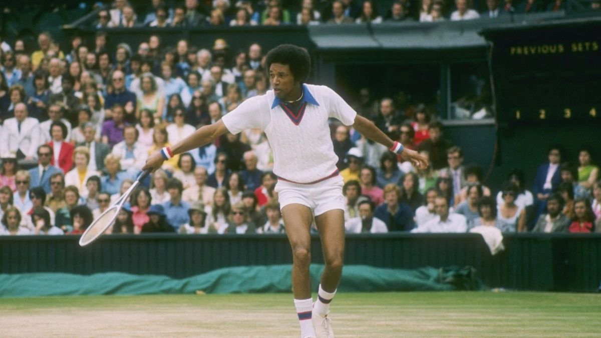 Arthur Ashe hits a backhand on a tennis court as the crowd looks on.