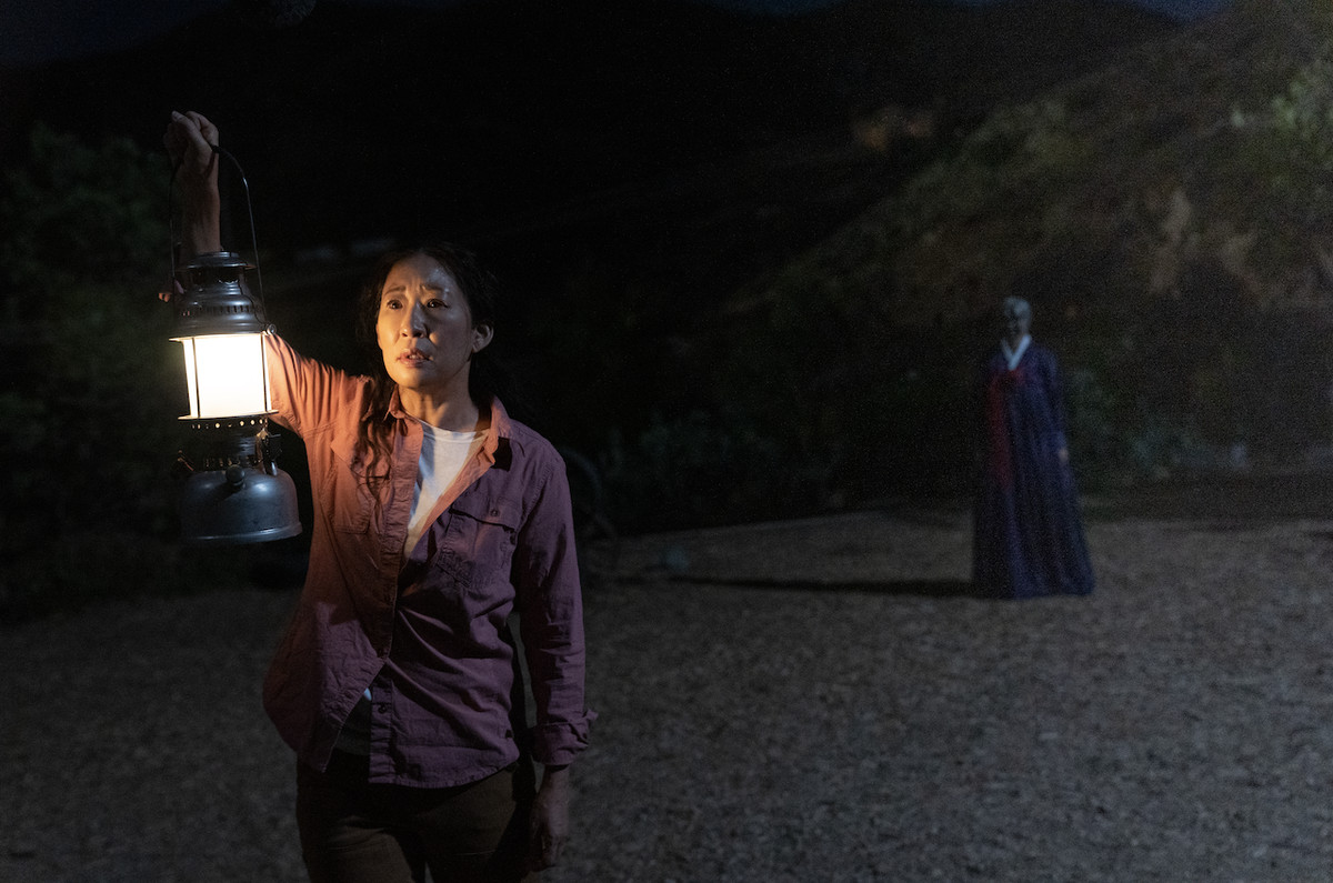 Sandra Oh as Beth holding a lantern outside as an ominous figure stands behind them in Umma.