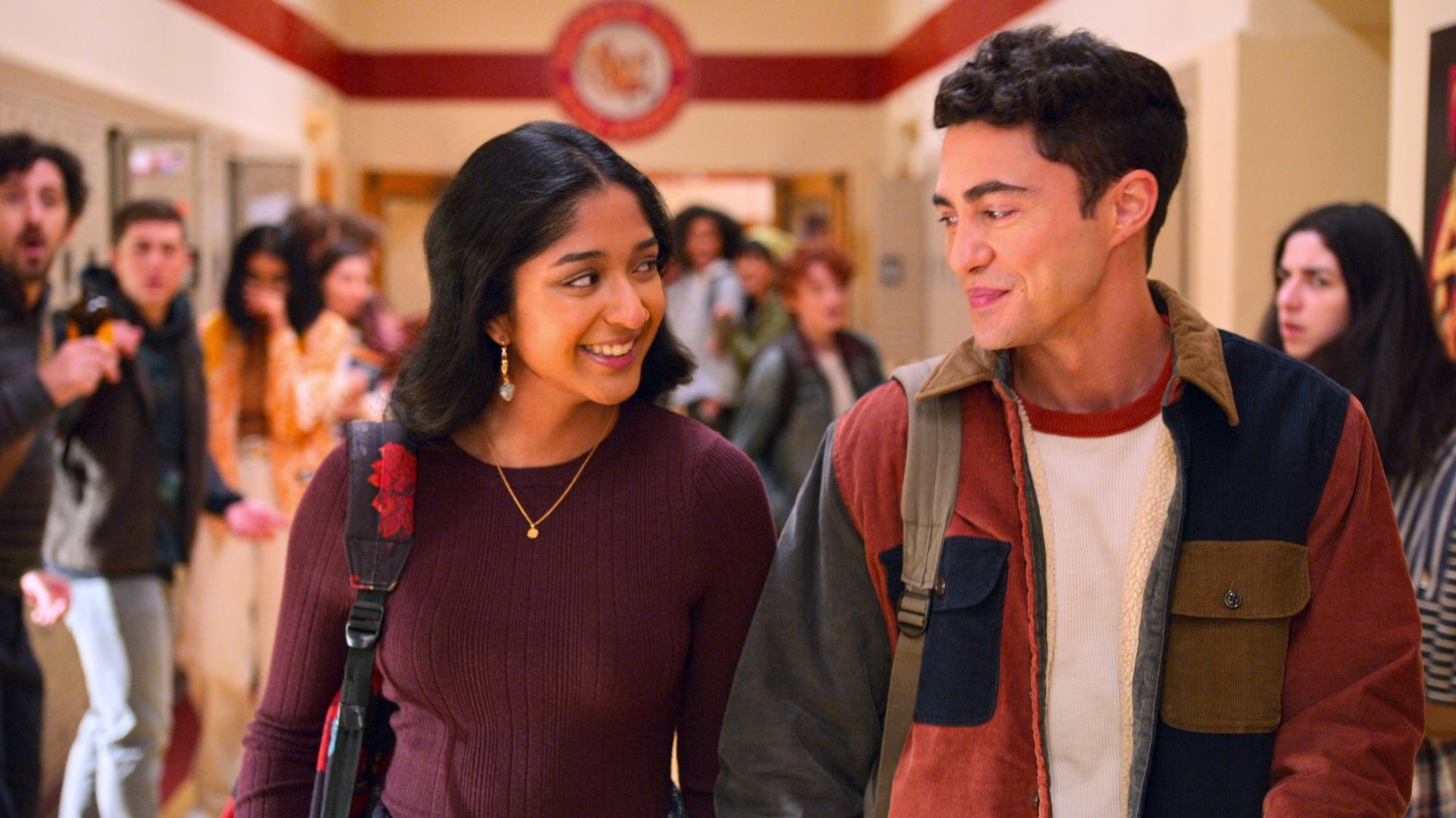 A young man and woman walk through a high school hallway holding hands.