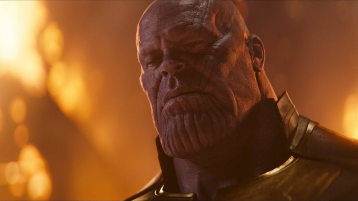 Thanos (Josh Brolin), a large purple alien with a large textured chin, stands in front of the burning wreckage of his attack on Earth.