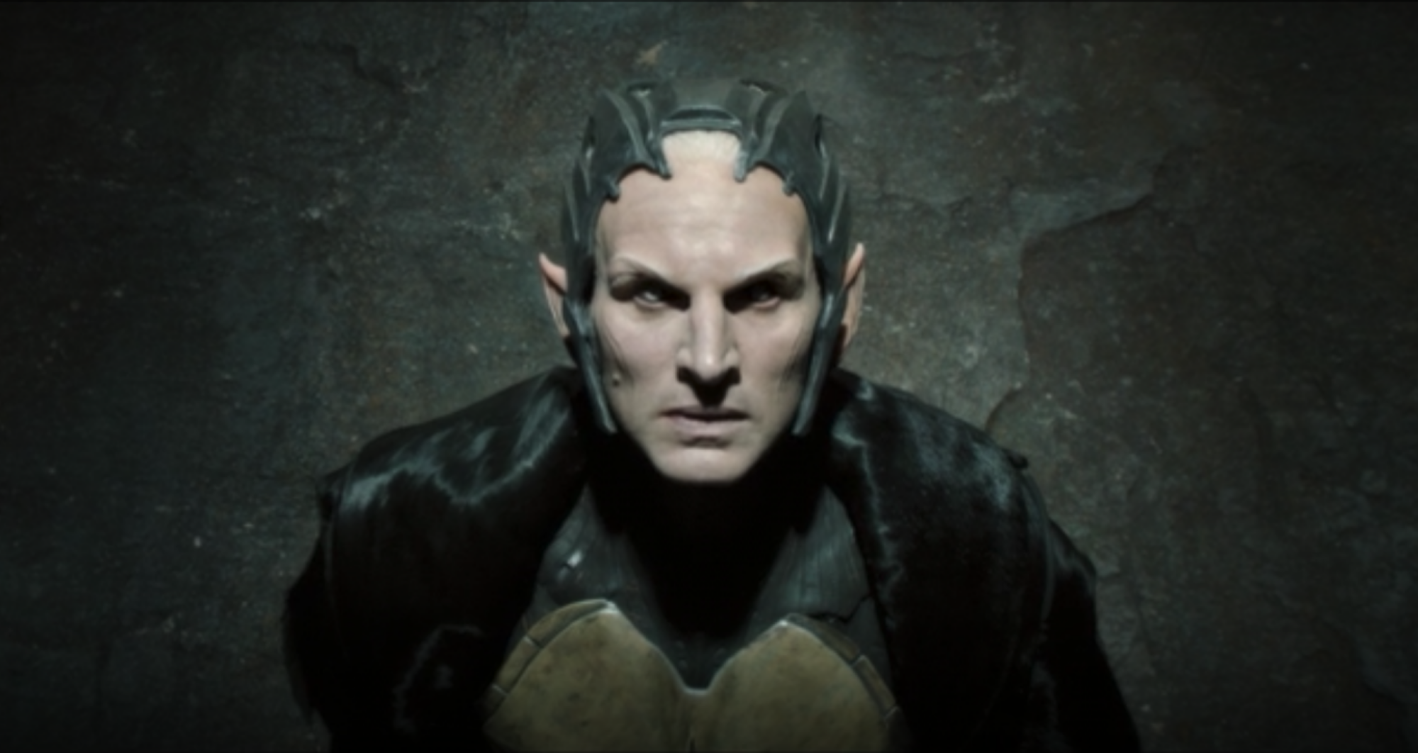 Close up of a pale, pointed figure with a sharp metal crown and dark robes: Malekith (Christopher Eccleston), the leader of the dark elves.