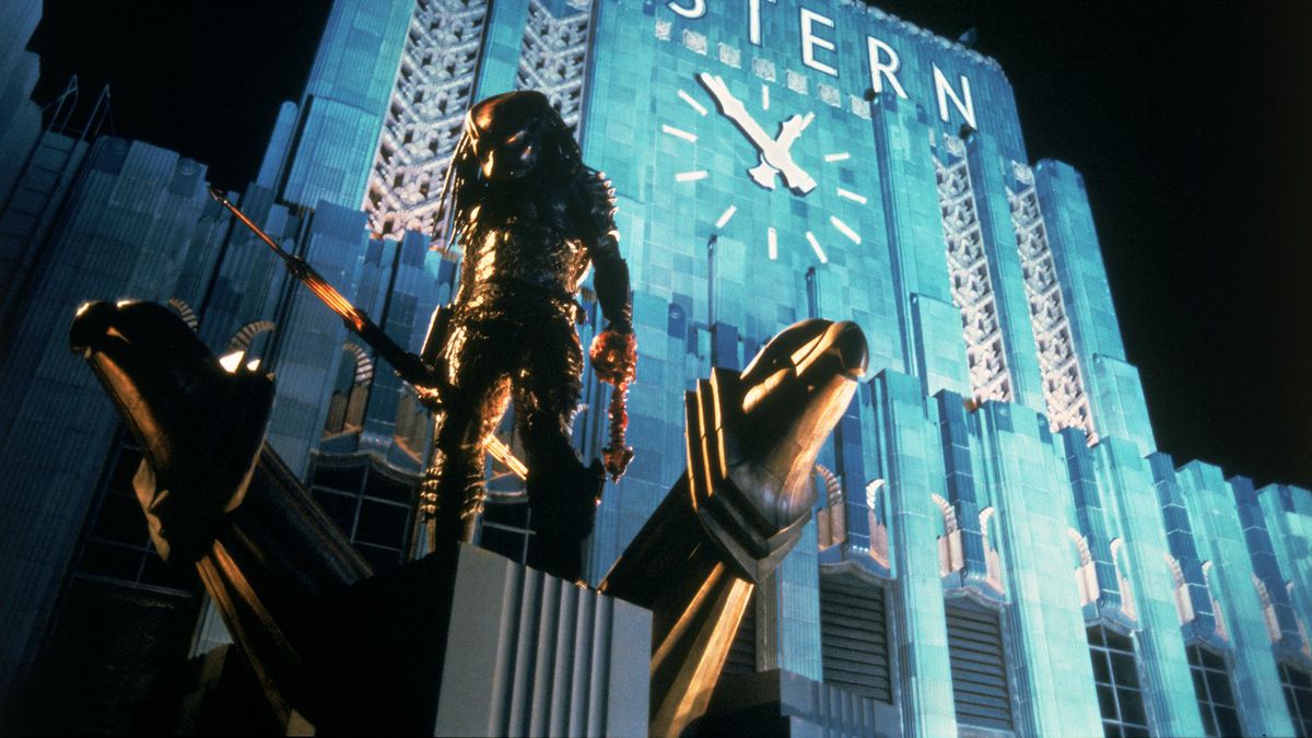 A Predator (Kevin Peter Hall) standing on the ledge of a skyscraper with human skull and spinal chord in their hand in Predator 2.