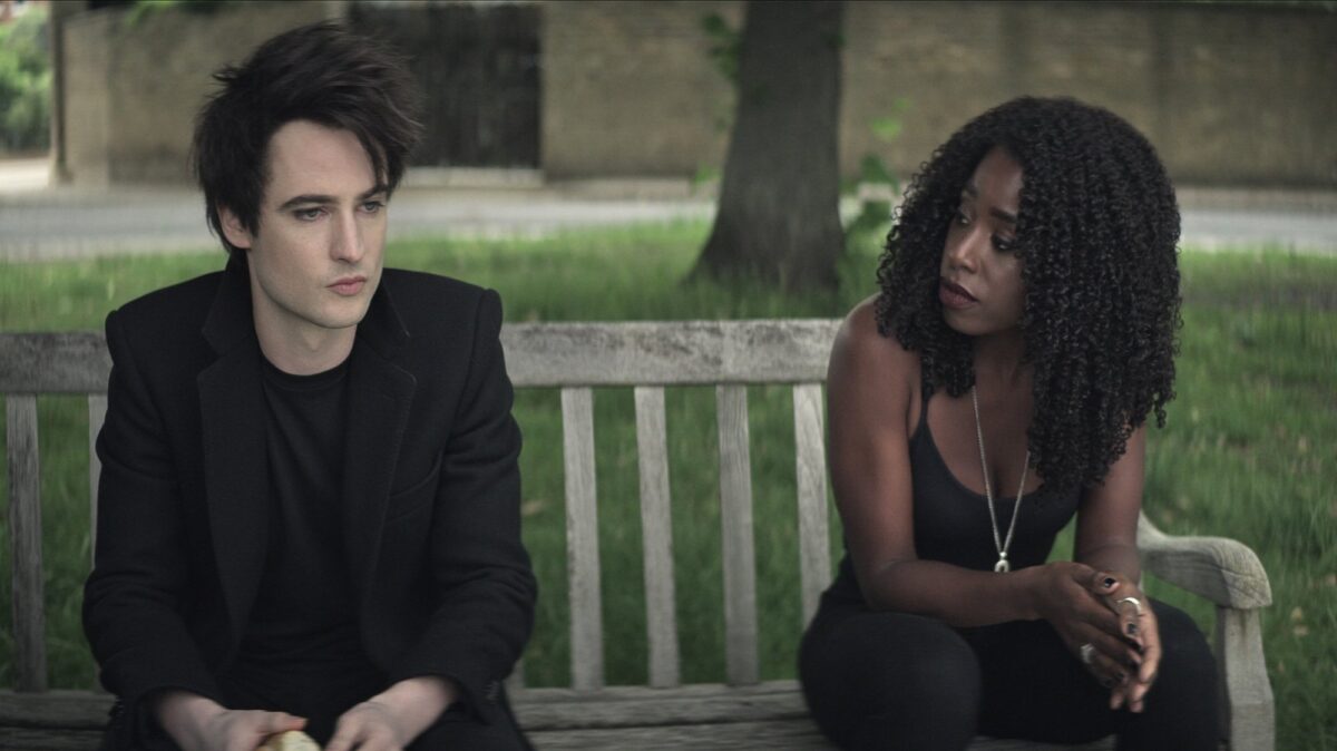 A man and woman dressed in black sit on a park bench.
