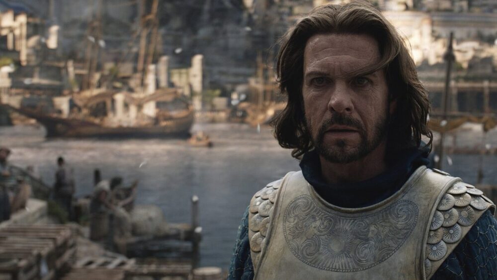 Elendil, a man in gold armor, stands with a harbor behind him.