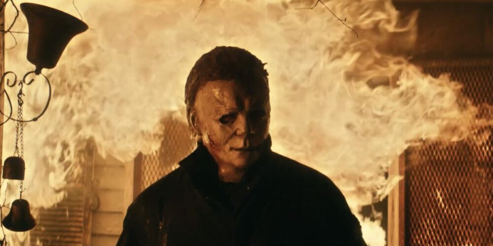 Michael Myers emerges from a burning house in Halloween Kills. The background is mostly flame.