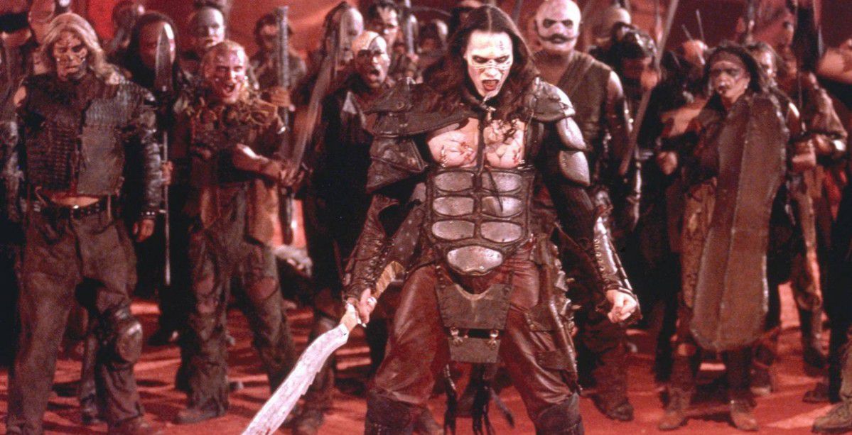 A long-haired warrior with pale skin dressed in armor and holding a swords stands in front of a horde of zombie-like soldiers.