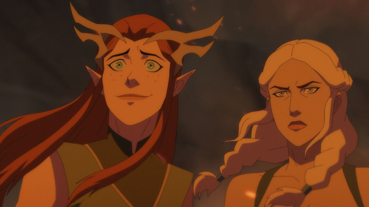 keyleth, a redhaired young woman, smiles nervously next to a pale-haired determined looking woman. they are both illuminated in a red glowing light