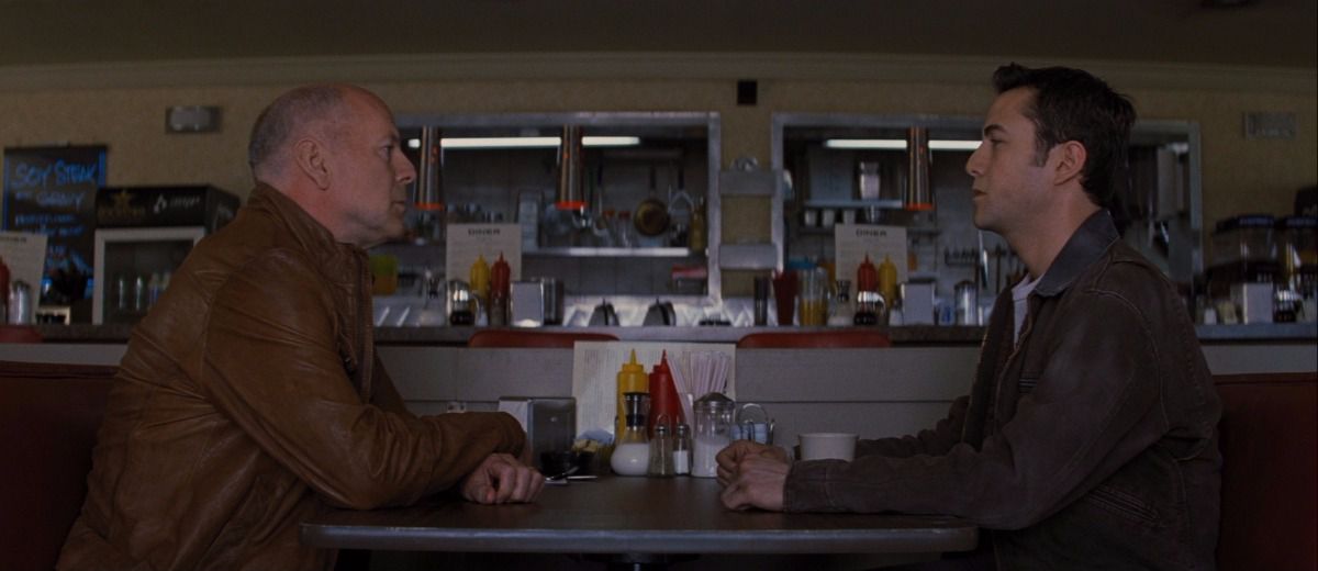 Bruce Willis (left) sits opposite of Joseph Gordon-Levitt (right) in prosthetic makeup in a roadside diner.