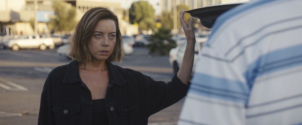 Aubrey Plaza as Emily stands by her car trunk, glaring at a prospective buyer in Emily the Criminal