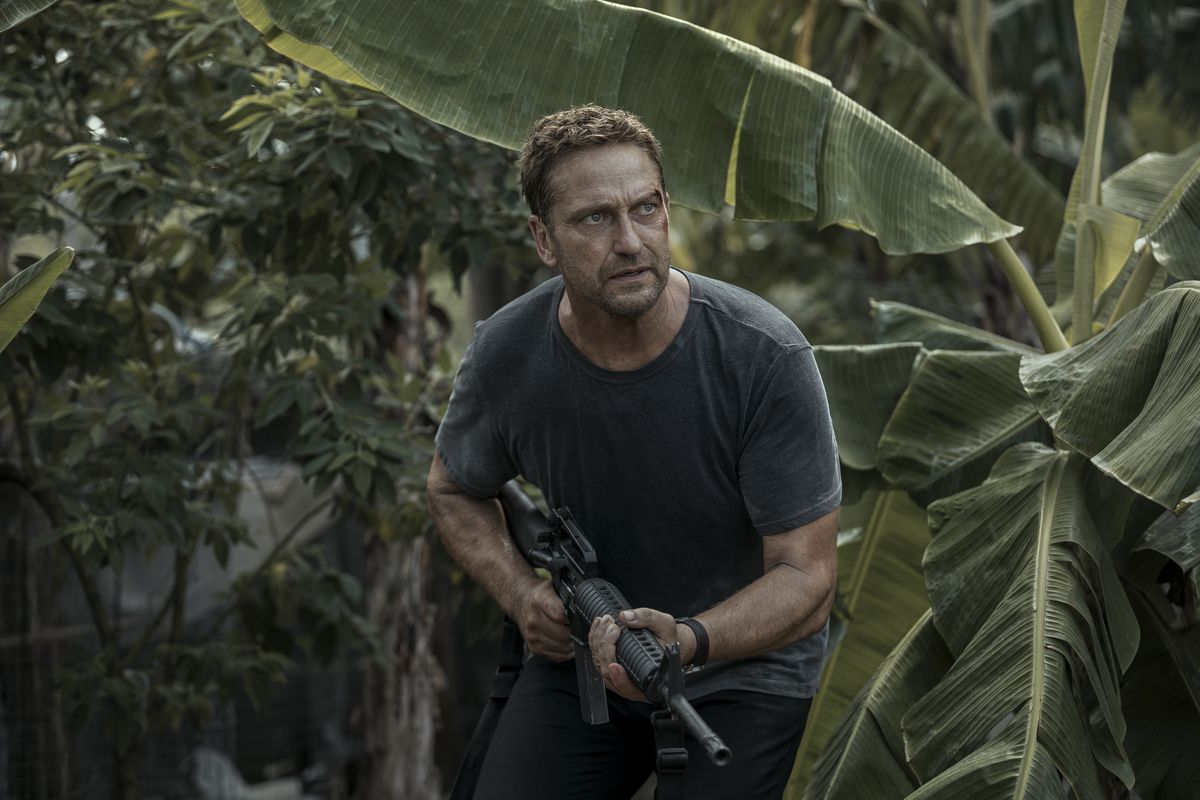 Gerard Butler’s Brodie, bleeding from the left side of his face, runs through the jungle with his gun in Plane