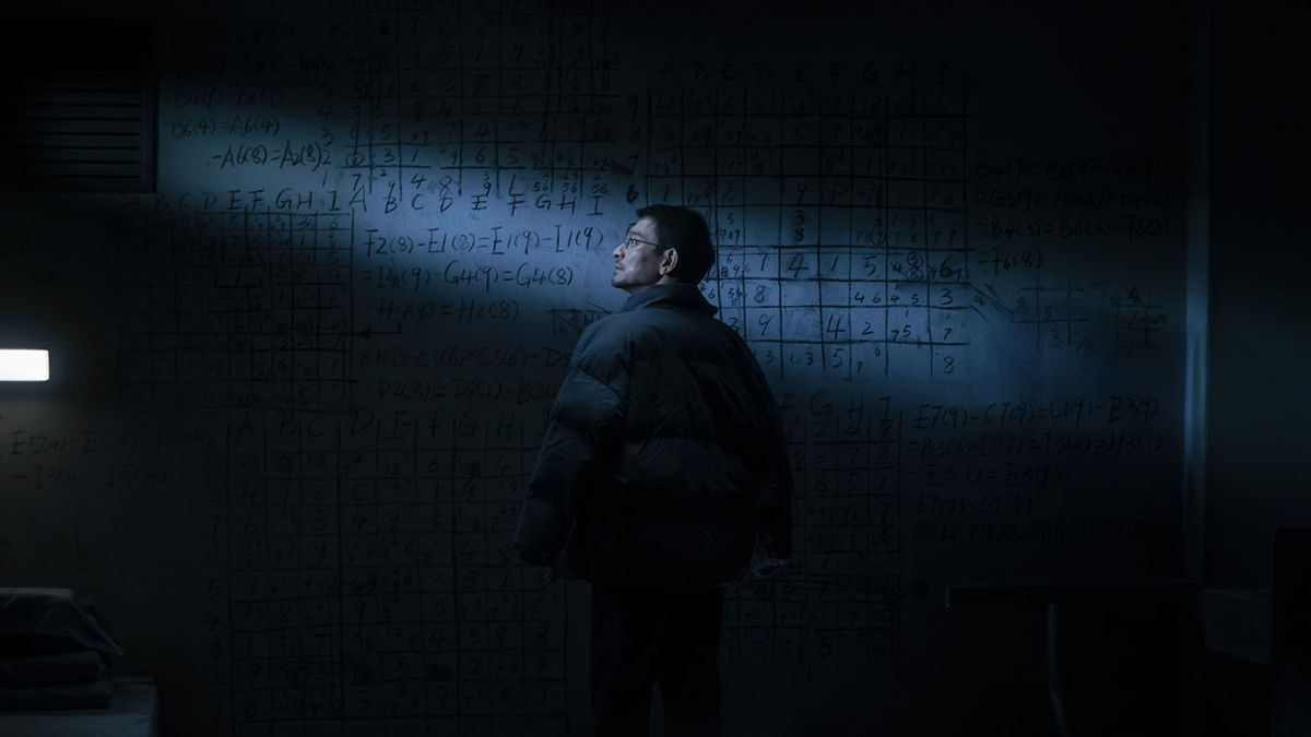 A man stands in a dark, chilly-looking room in front of an immense blackboard covered with mathematical symbols and formulae, dimly lit by a single shaft of light, in The Wandering Earth II