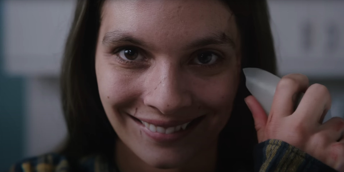 A character in the movie Smile with a wide grin and a shard of glass