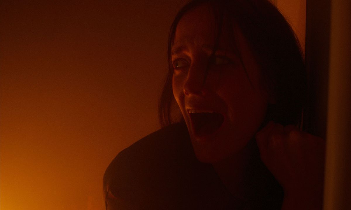 A screaming woman (Eva Green) leans against a wall away from a red, fire-like glow off-screen.