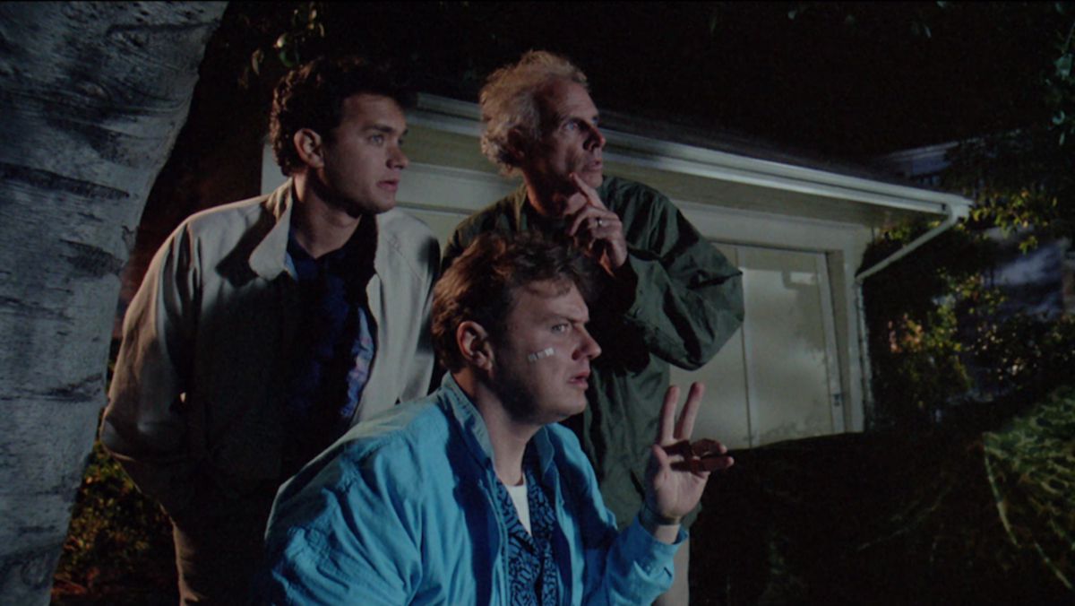 Three men (L-R Tom Hanks, Rick Ducommun, Bruce Dern) hide behind a trashcan at nighttime, staring at something offscreen.
