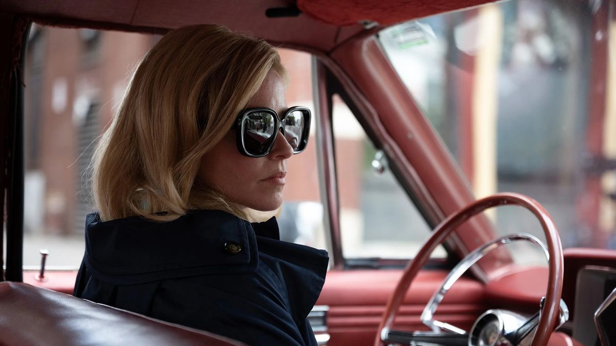 A woman (Elizabeth Banks) wearing sunglasses and seated behind the wheel of a red convertible in Call Jane