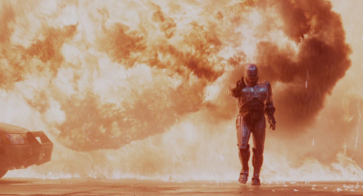 Robocop aiming his automatic pistol while walking away from a massive plume of fire in Robocop.