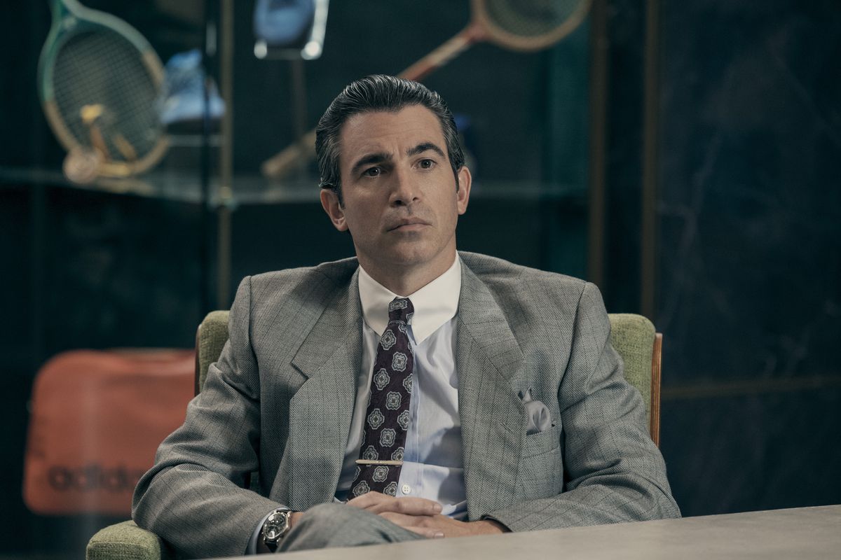 Chris Messina as David Falk sits in a corporate meeting room in a grey suit in the film Air.