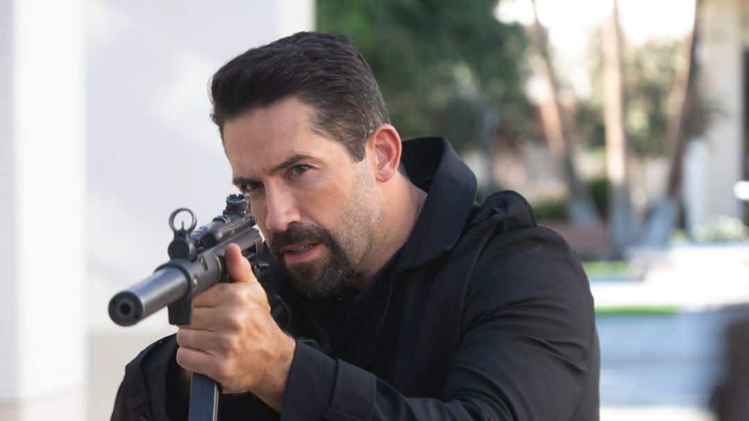 Scott Adkins — a man with a goatee and black coat — aiming a rifle in Section 8.