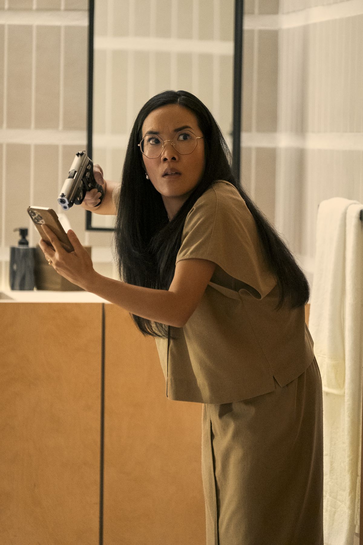 Amy (Ali Wong) holding a gun at a phone in her hand and looking shocked at something off-camera