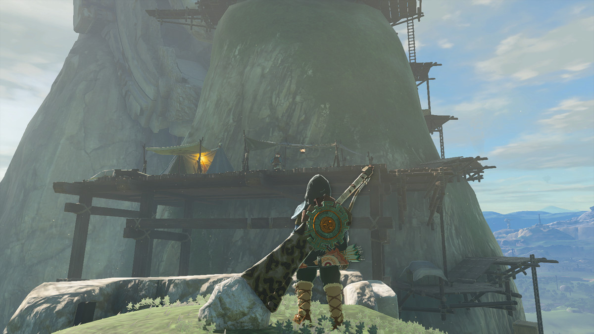 Link looks at a survey camp in The Legend of Zelda: Tears of the Kingdom. There is scaffolding built into a rocky hillside.