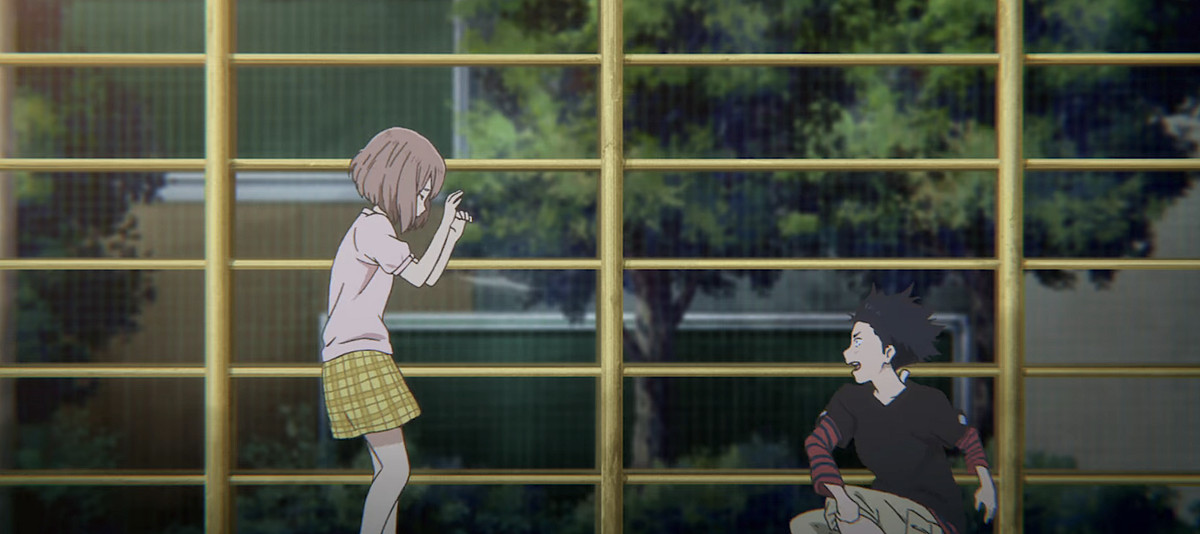 Spiky-haired grade-school boy Shôya Ishida throws dirt at Deaf classmate Shoko Nishimiya and yells at her in front of a grid of yellow fencing in a flashback scene in A Silent Voice
