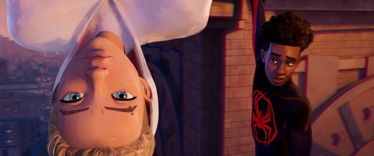 Gwen Stacy hangs upside down from a building in the foreground while Miles Morales smiles at her from the background in the animated movie Spider-Man: Across the Spider-Verse