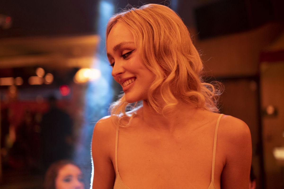 Mid shot of Lily Rose-Depp as the pop star Jocelyn smiling at someone off camera under a club’s red lights in the HBO series The Idol