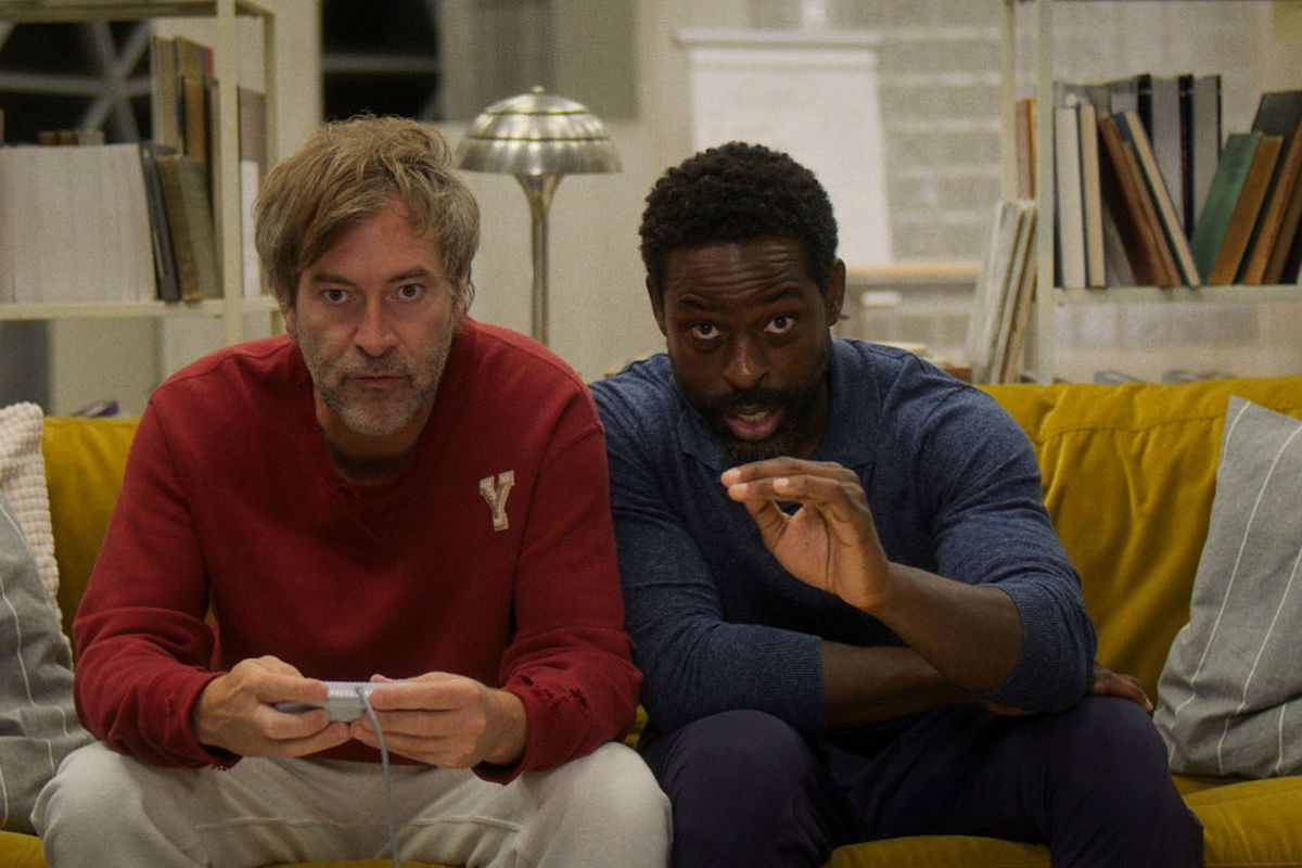 (L-R) Mark Duplass and Sterling K. Brown sitting on a couch and playing a videogame in Biosphere.