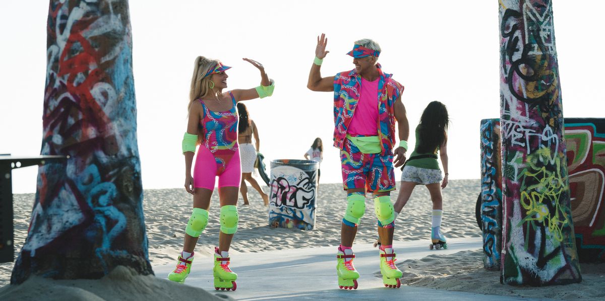 Barbie (Margot Robbie) and Ken (Ryan Gosling), both wearing garish, patterned neon skating outfits and incredibly bright neon-yellow kneepads and Rollerblades, stand in front of a beach between two trees covered in graffiti and go in for a high five in the 2023 live-action movie Barbie
