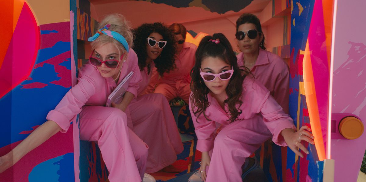 The back of a garishly neon-painted panel van opens to reveal four women in matching powder-pink jumpsuits and non-matching pink-rimmed sunglasses: Barbie (Margot Robbie), also Barbie (Alexandra Shipp), Sasha (Ariana Greenblatt), and Gloria (America Ferrera), in the live-action 2023 movie Barbie