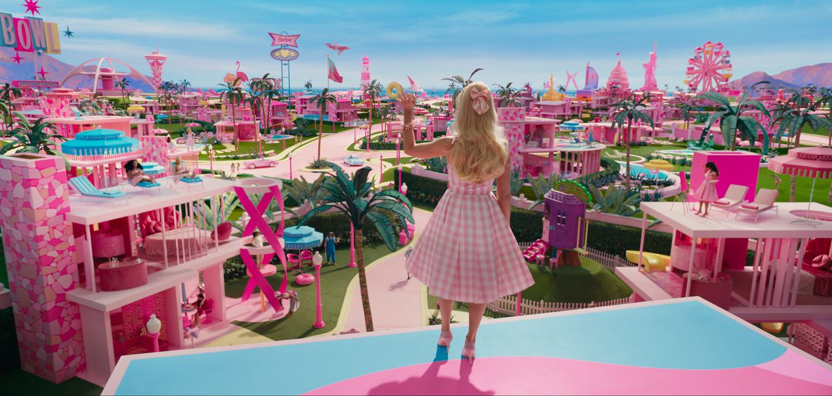 Barbie (Margot Robbie), seen from behind, stands on the pink-and-blue plastic roof of her DreamHouse and looks out over all the other pink plastic DreamHouses of the other Barbies in Barbieland, in the live-action 2023 movie Barbie
