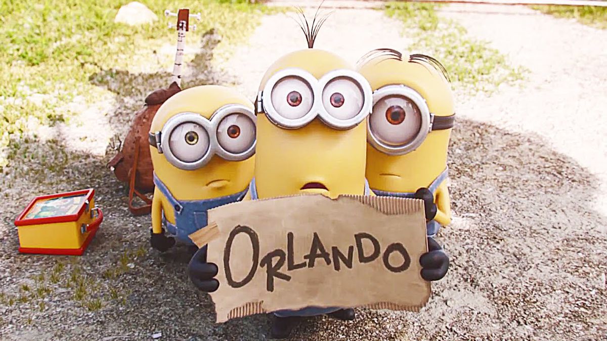 Three Minions holding a cardboard sign that says “Orlando,” as they hitchike