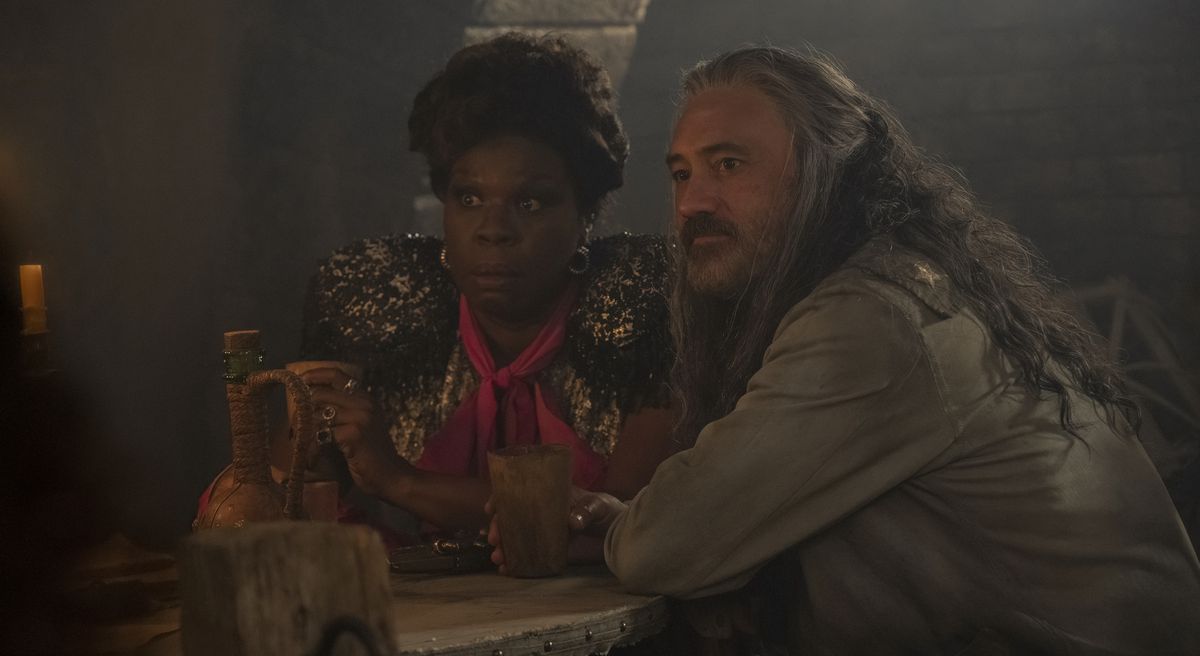 Spanish Jackie (Leslie Jones, looking shocked) and Blackbeard (Taika Waititi, looking calm) sit at a table together in Jackie’s bar and stare at something offscreen in season 2, episode 7 of Our Flag Means Death