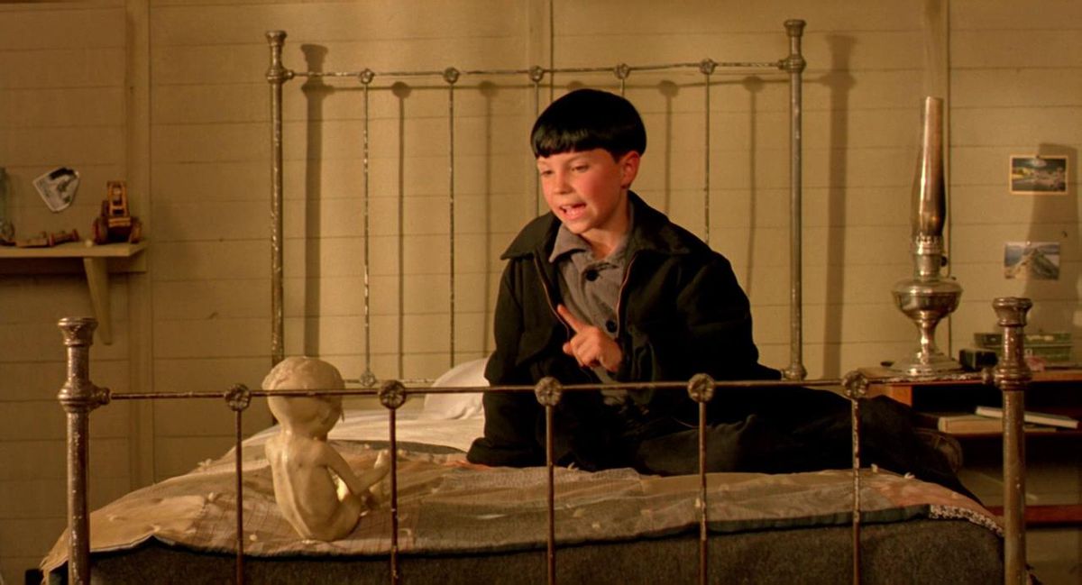 A young boy talks to what looks like a clay fetus in a bed in The Reflecting Skin.