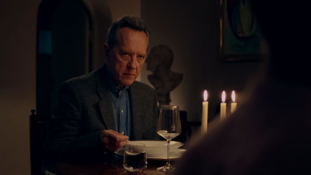 Richard E. Grant sits at a dinner table and looks severe in The Lesson.