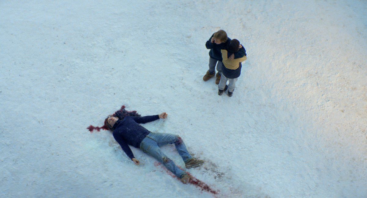 A dead, bloody body in the snow in Anatomy of a Fall, as someone near talks on the phone