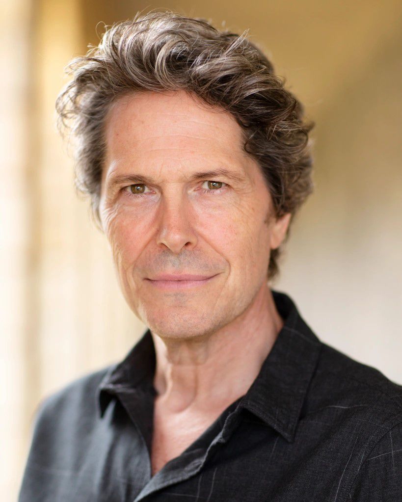 A headshot of actor Neil Roberts, a handsome middle aged man with swoopy greying hair