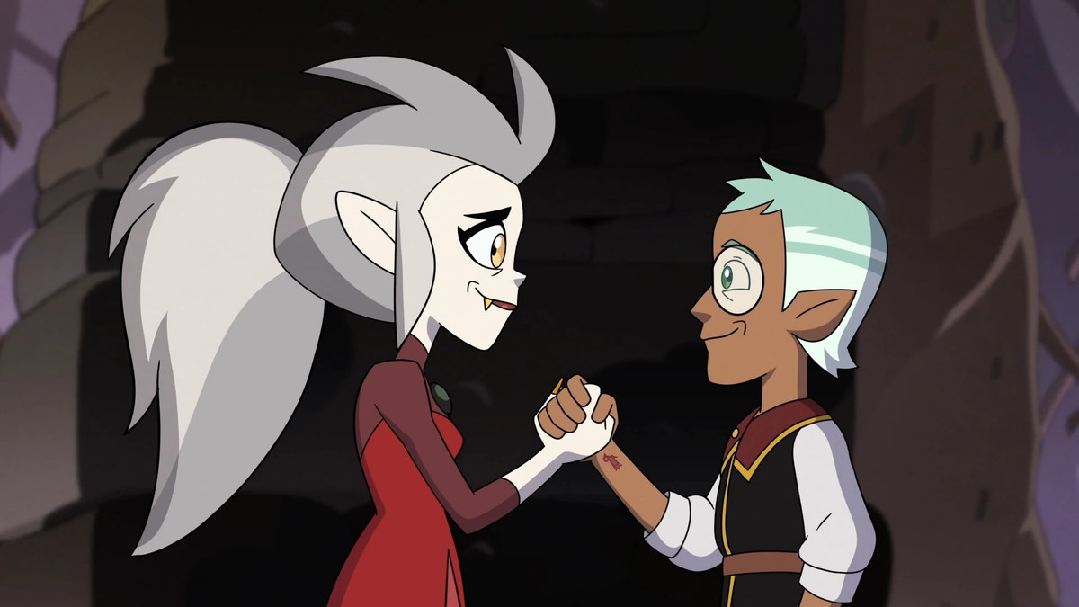 An image of Eda and Raine from Owl House looking at each other. They’re standing facing each other as they grip the other’s hand and are smiling.