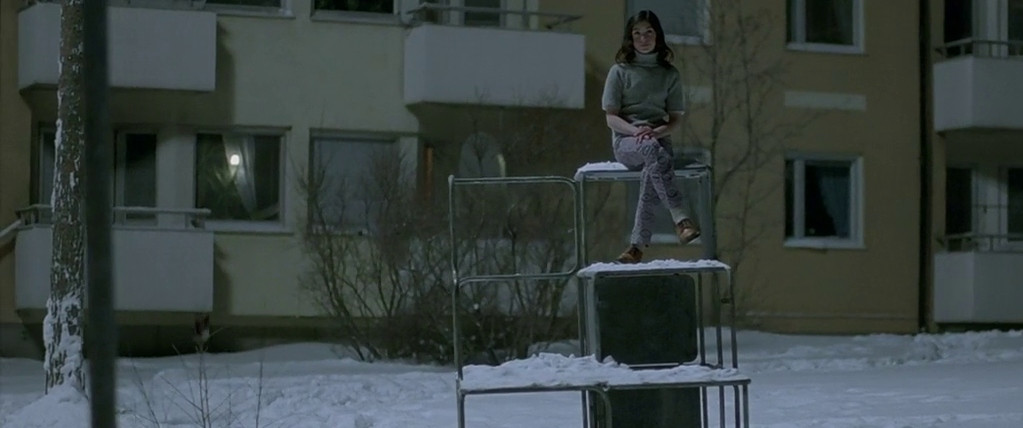 لینا لندرسون در فیلم Let the Right One In بر بالای یک مجسمه یخ زده نشسته است.