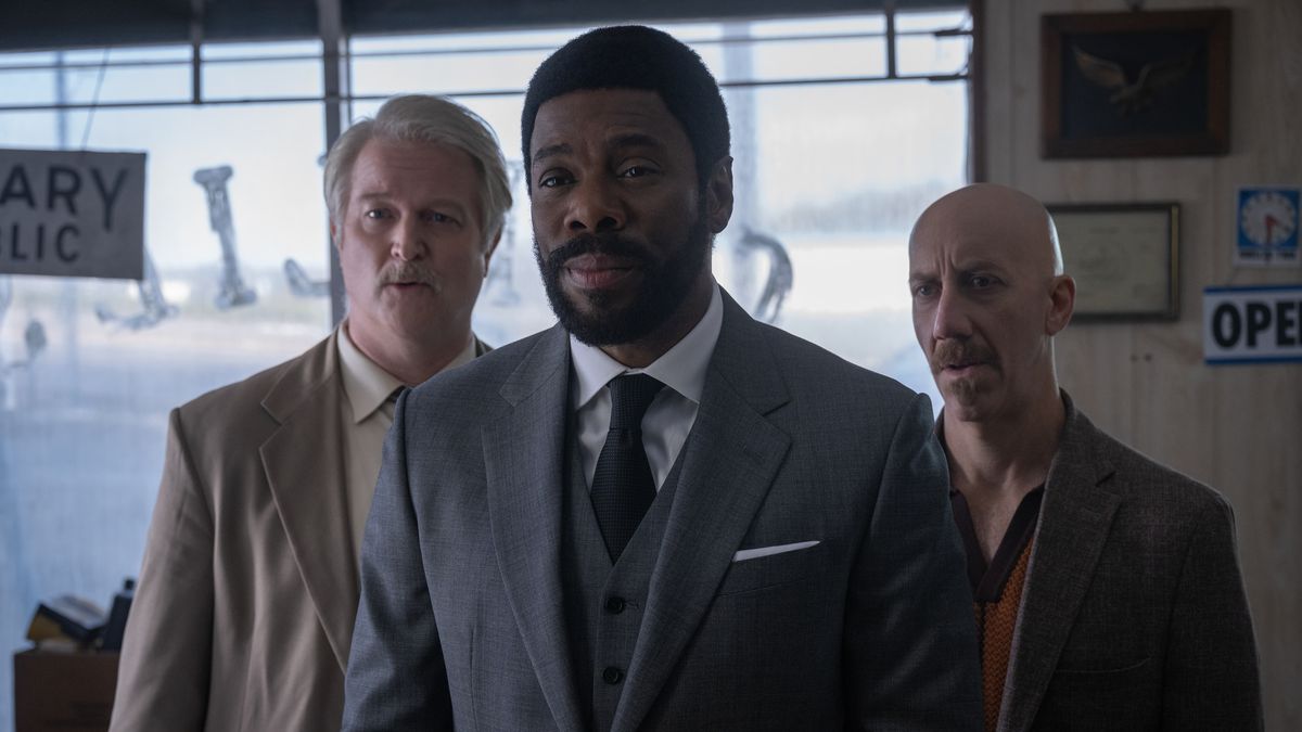 Colman Domingo as The Chief and his two henchmen stand in an auto garage in a scene from Drive-Away Dolls. 